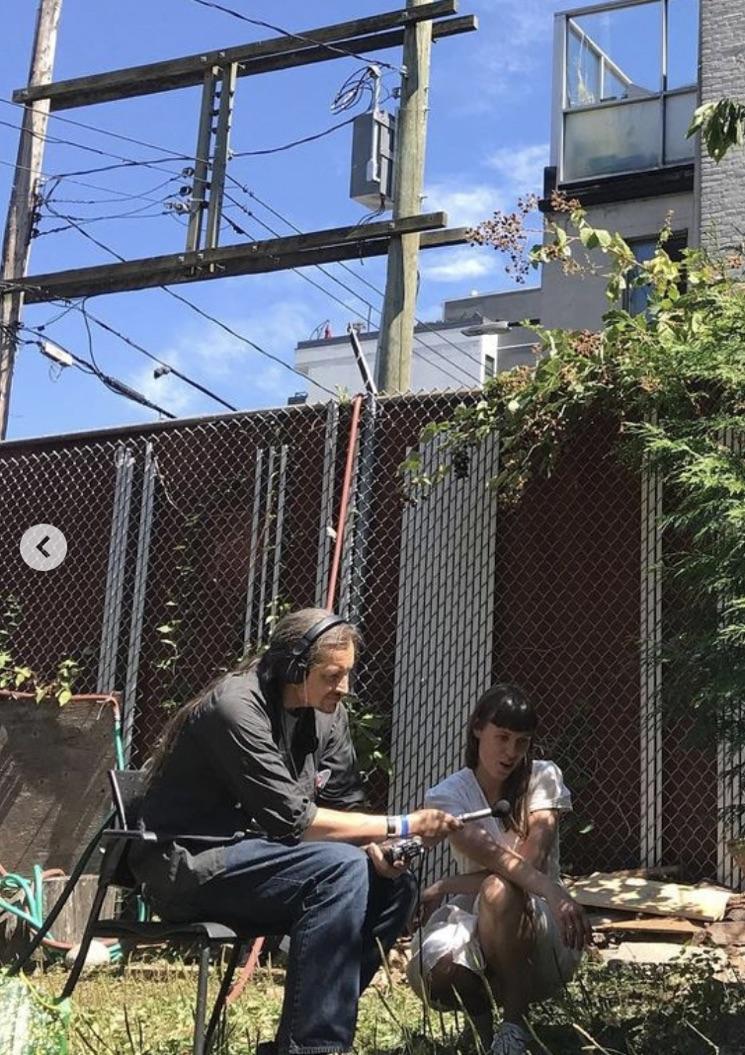 Two people sit in a garden, one wearing headphones recording their surroundings.
