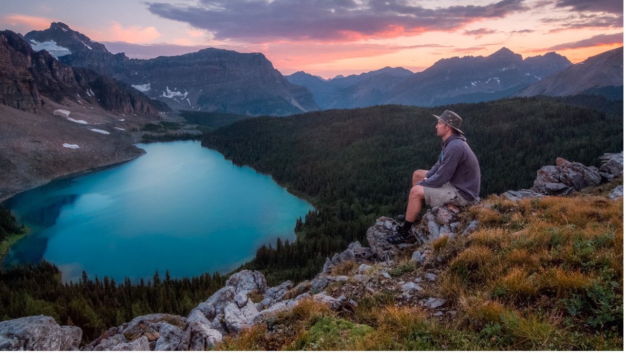 Man sitting at the edge of a cliff looking towards a lake